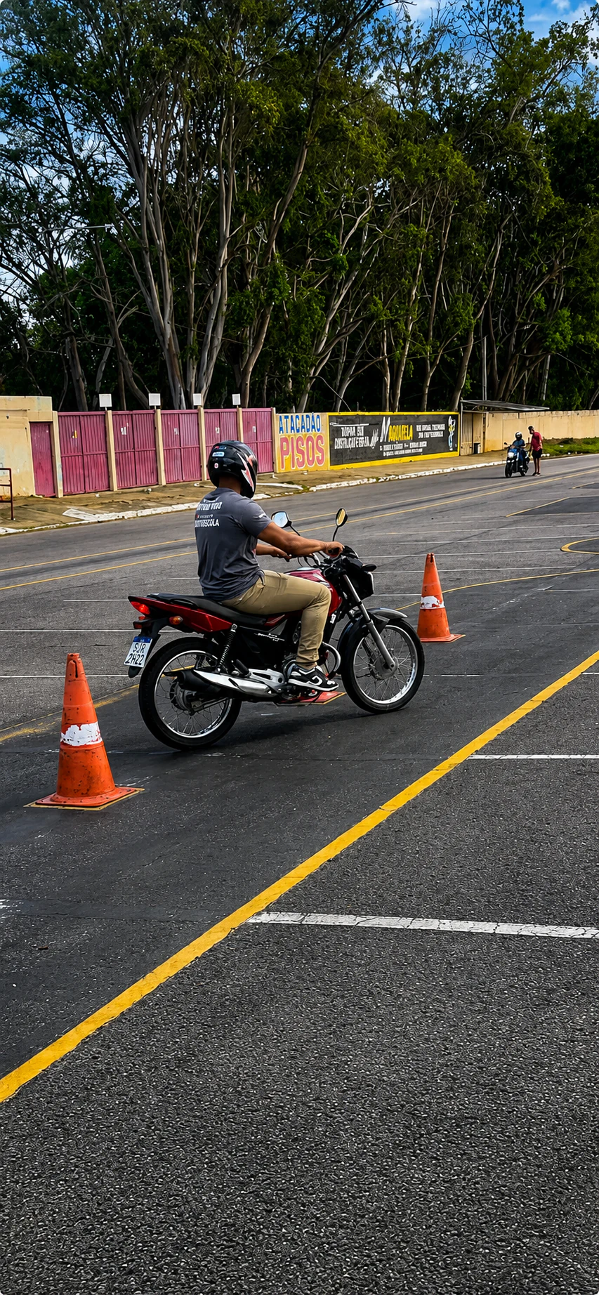 Instrutor conduzindo uma motocicleta entre cones no circuito da prova prática