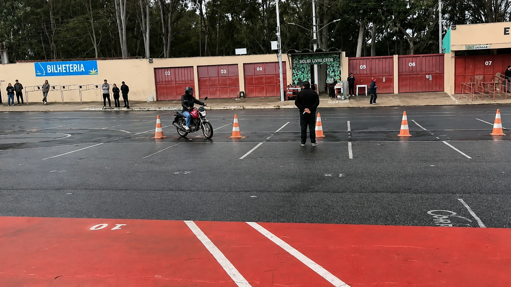 Candidato realizando o percurso da prova prática de moto diante do examinador em uma pista com cones