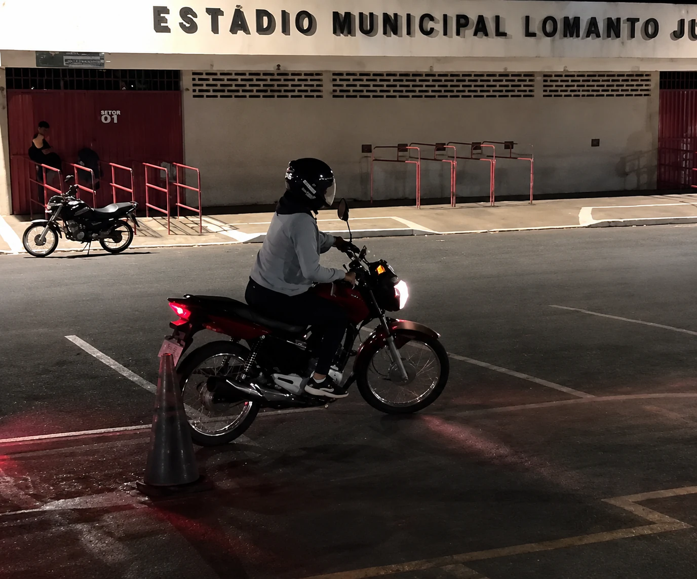 Aluna conduzindo uma motocicleta ao lado de um cone durante o treinamento noturno